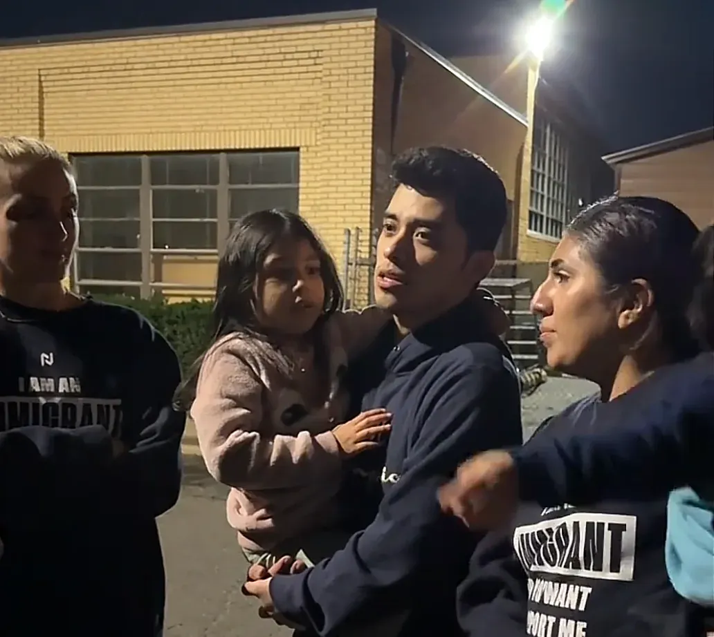 a man holding his daughter and standing next to his wife, talking to reporters. 
